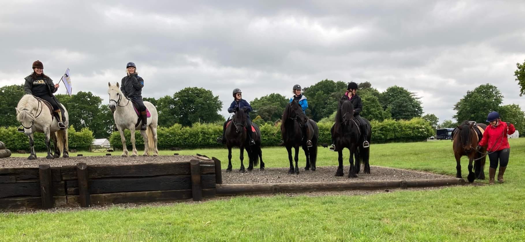 six ponies and riders by a cross country jump