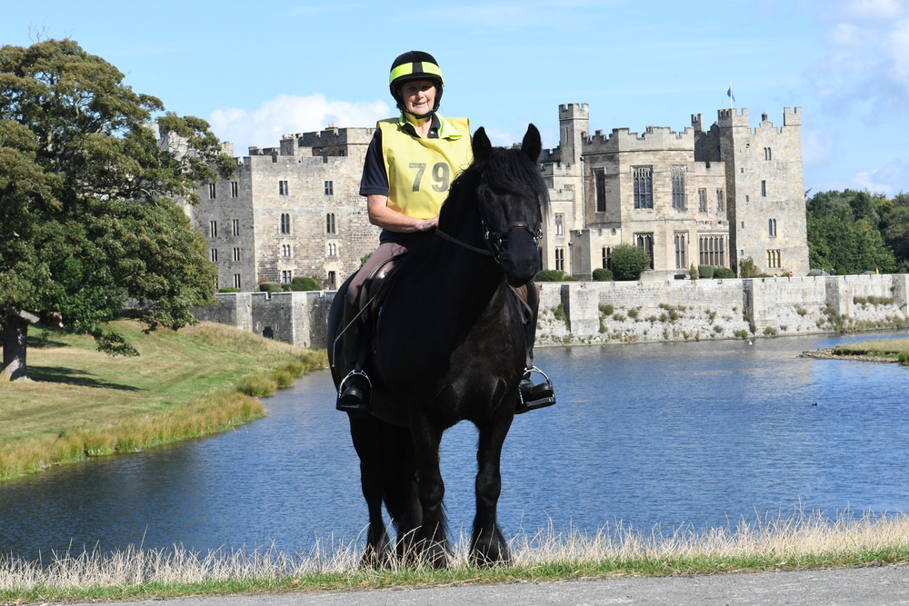 black pony and rider in front of a lake and large country house